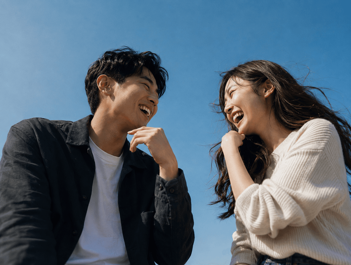 Two people laughing together under a blue sky